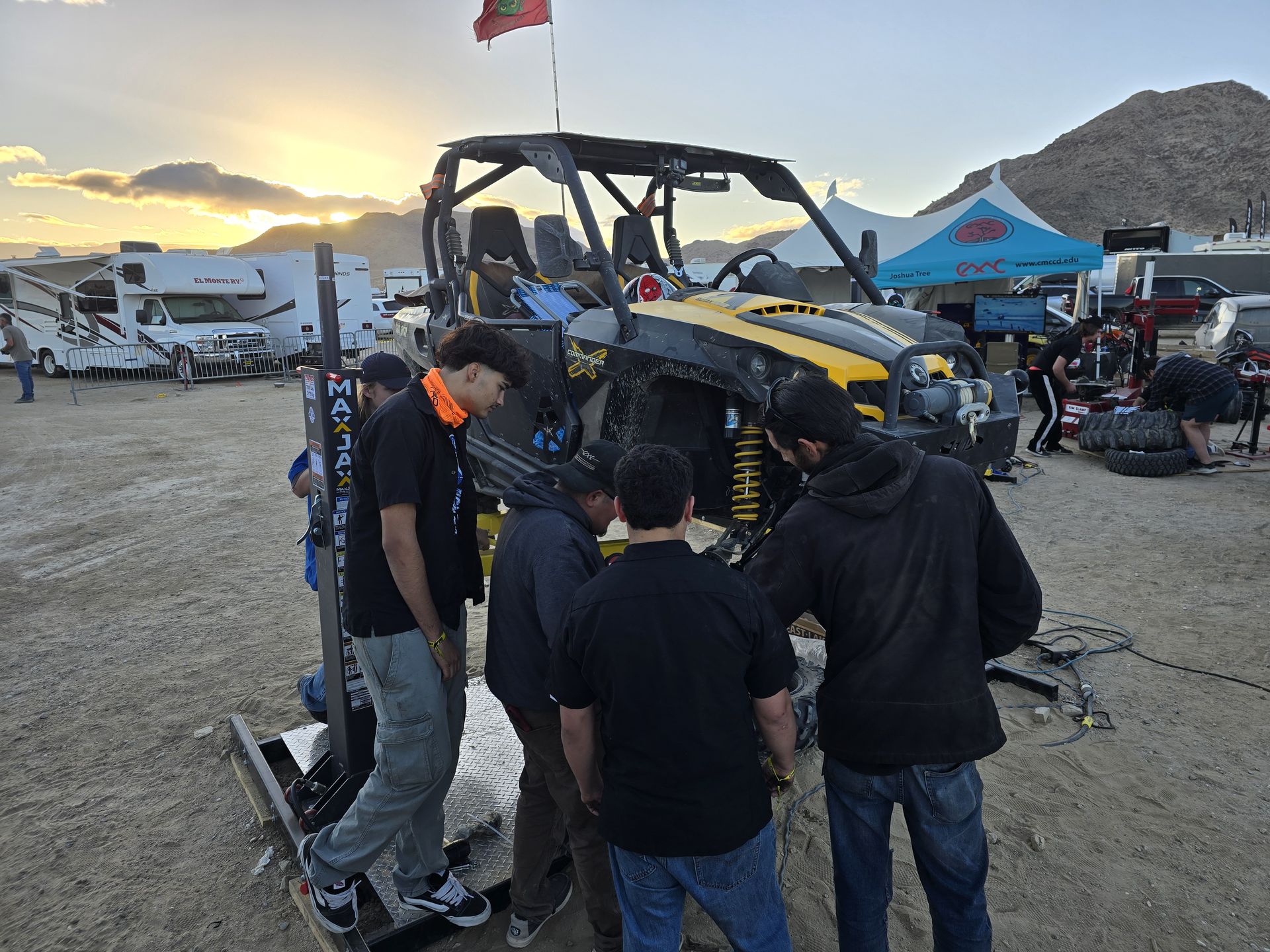 Students working on a race UTV on a lift at sunset