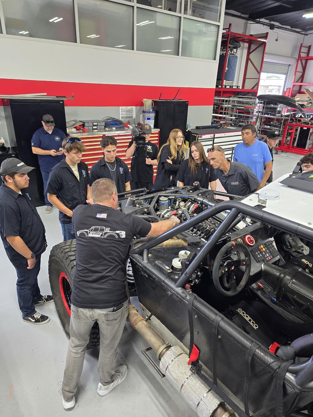 Students and professional fabricators around a race truck chassis during the 1Nine Industries shop tour
